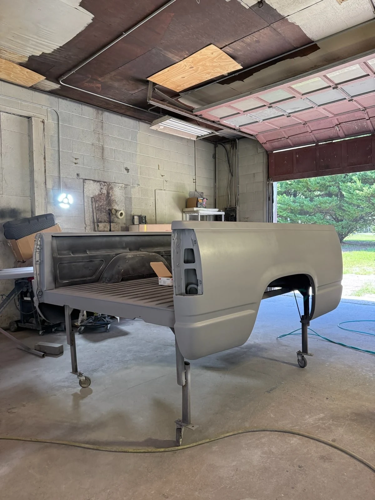 Detached pickup truck bed in gray primer on repair stands before final refinishing in the Gordonsville shop