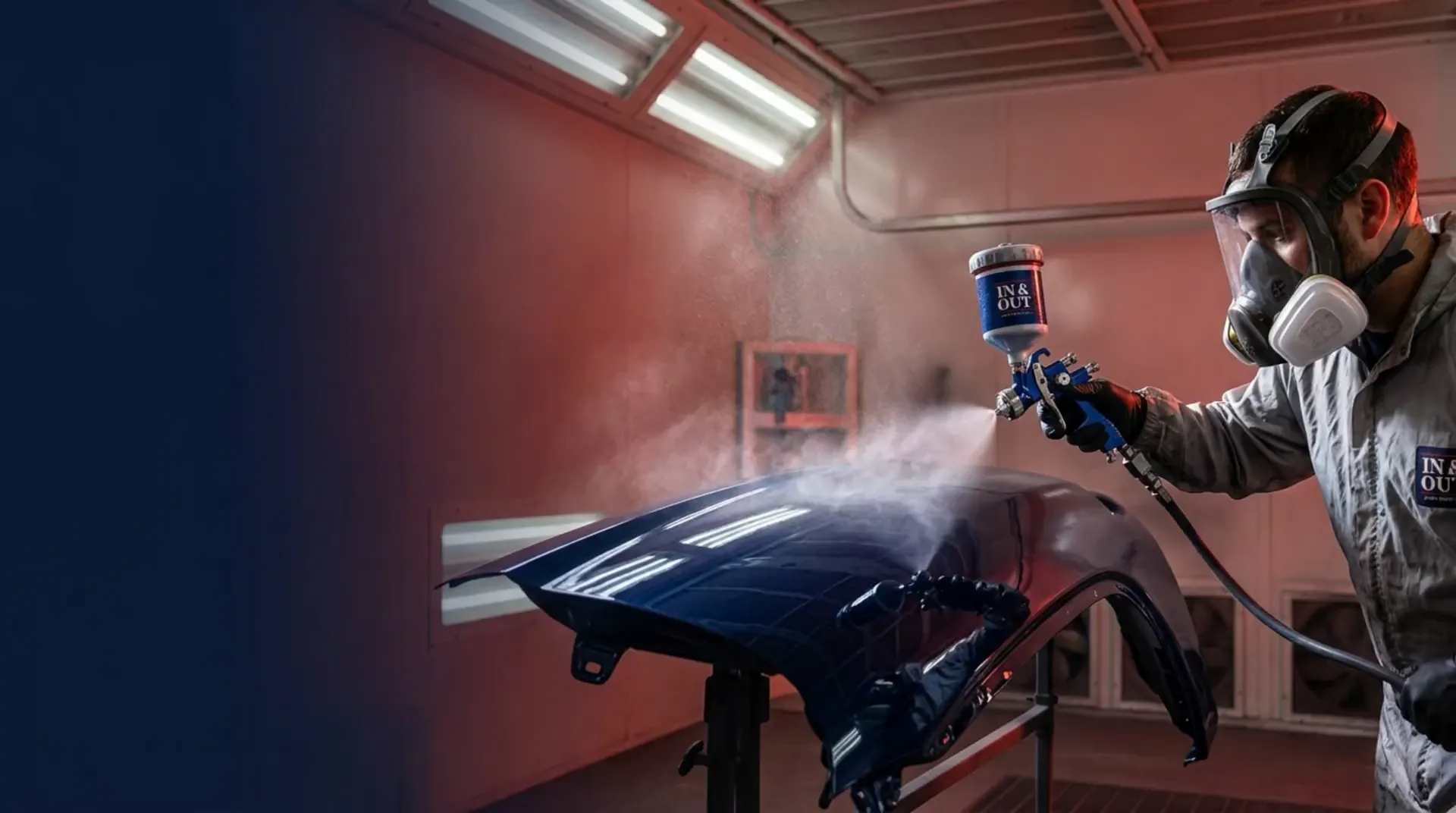 Auto body technician spray-painting a glossy navy car fender with an HVLP gun inside a lit paint booth in Gordonsville VA
